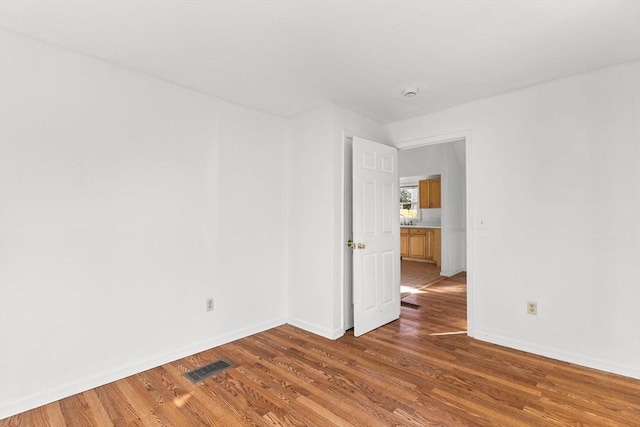 unfurnished room with visible vents, a sink, baseboards, and wood finished floors