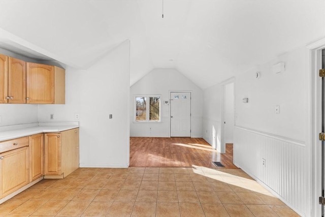 kitchen featuring light tile patterned floors, visible vents, lofted ceiling, light countertops, and wainscoting