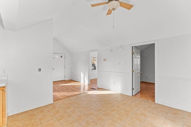 empty room with light tile patterned floors, lofted ceiling, a ceiling fan, and wainscoting