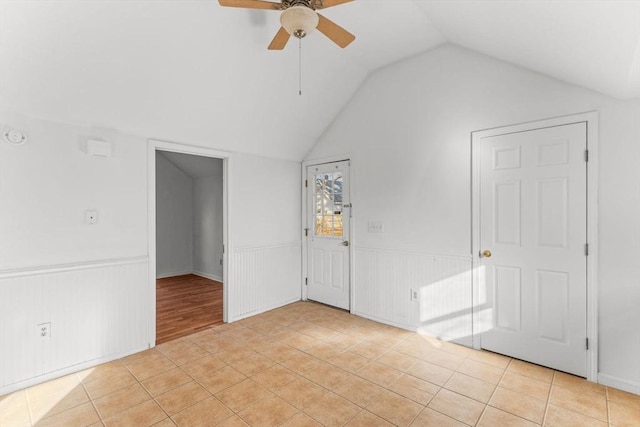 spare room featuring vaulted ceiling, light tile patterned flooring, a wainscoted wall, and ceiling fan