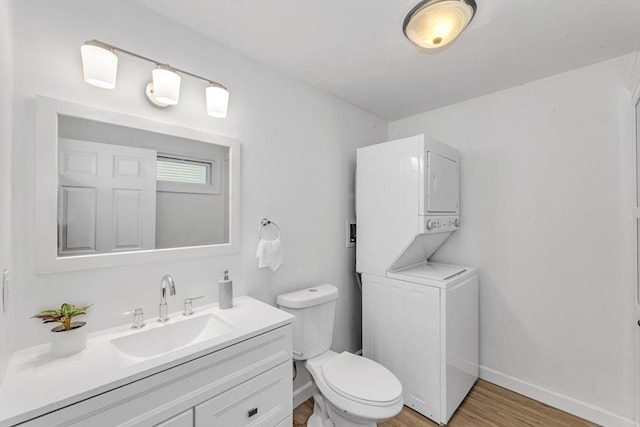 bathroom with stacked washer / drying machine, toilet, wood finished floors, baseboards, and vanity