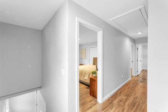 corridor featuring attic access, light wood finished floors, and baseboards
