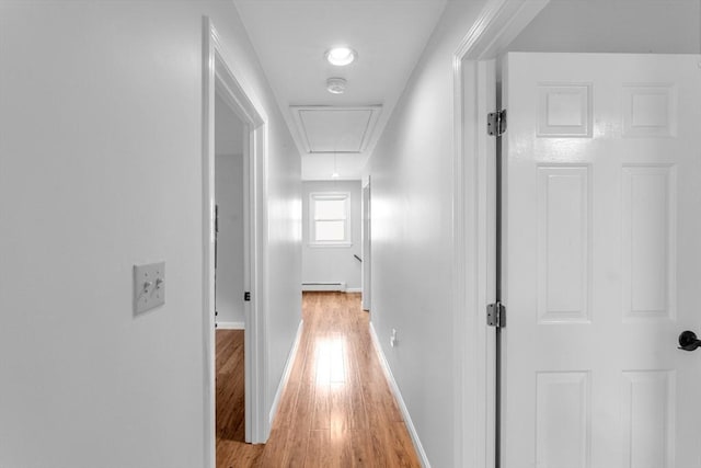 hallway featuring attic access, light wood-type flooring, a baseboard heating unit, and baseboards