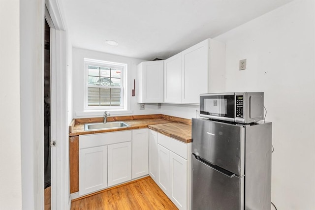 kitchen featuring appliances with stainless steel finishes, a sink, butcher block counters, light wood finished floors, and white cabinets