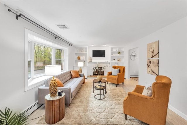 living area with a baseboard heating unit, built in shelves, light wood-style flooring, and baseboards