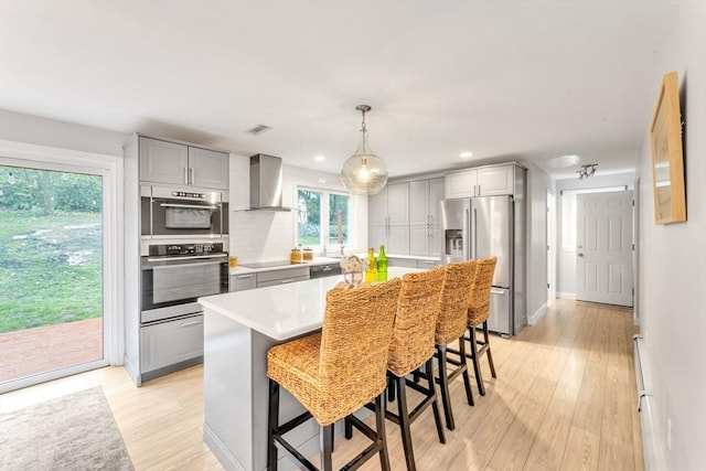 kitchen with appliances with stainless steel finishes, wall chimney range hood, gray cabinets, light countertops, and light wood finished floors