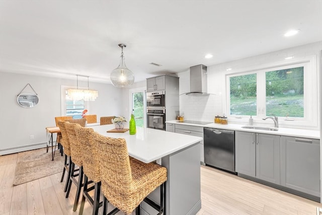 kitchen with dishwasher, gray cabinetry, wall chimney range hood, a sink, and double wall oven
