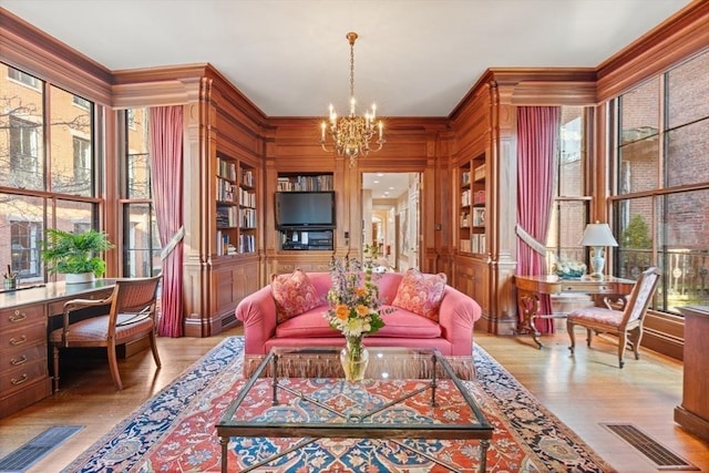 sitting room with ornamental molding, light wood-type flooring, built in features, and a notable chandelier