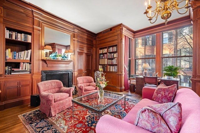 sitting room featuring built in shelves, light hardwood / wood-style floors, wooden walls, and a chandelier