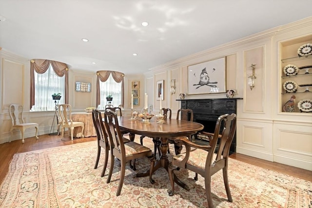 dining room with built in shelves, wood-type flooring, and ornamental molding