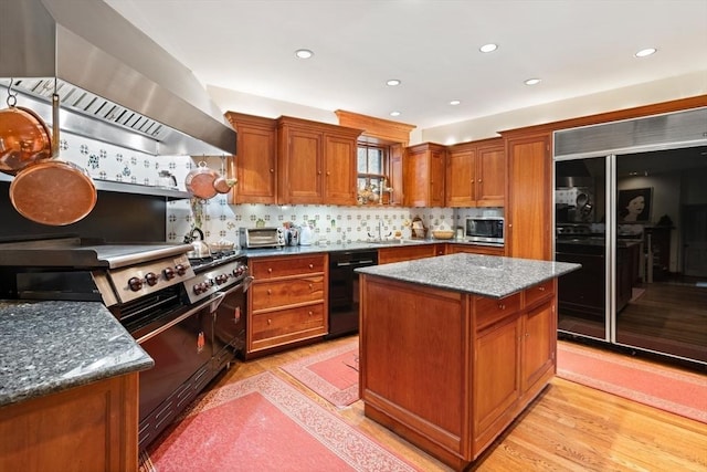 kitchen featuring backsplash, dark stone counters, black appliances, wall chimney range hood, and a kitchen island