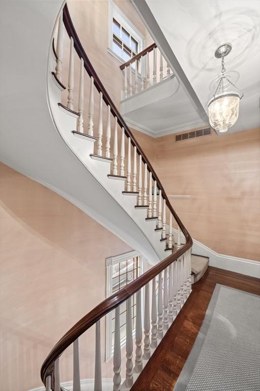 staircase with a wealth of natural light, wood-type flooring, a notable chandelier, and ornamental molding