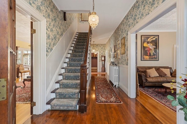 foyer entrance with stairs, wood finished floors, wainscoting, and wallpapered walls