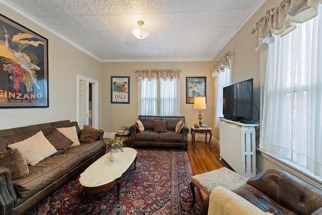 living room featuring crown molding, baseboards, wood finished floors, and radiator