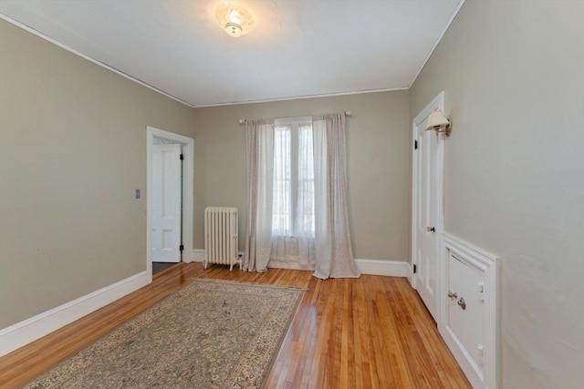 interior space featuring ornamental molding, light wood finished floors, radiator heating unit, and baseboards