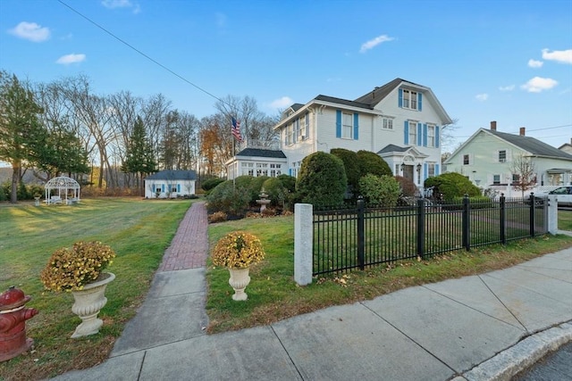 view of front of home with a fenced front yard, a front lawn, and an outbuilding