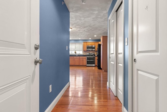 corridor with light wood-type flooring and a textured ceiling