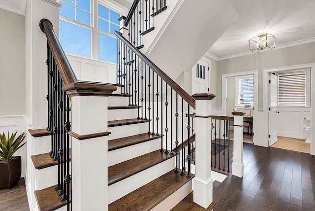 staircase with an inviting chandelier, ornamental molding, and hardwood / wood-style flooring