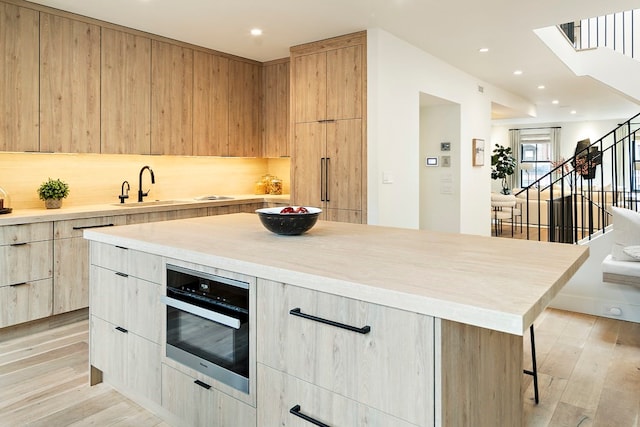 kitchen featuring oven, sink, a kitchen island, a breakfast bar area, and light hardwood / wood-style flooring