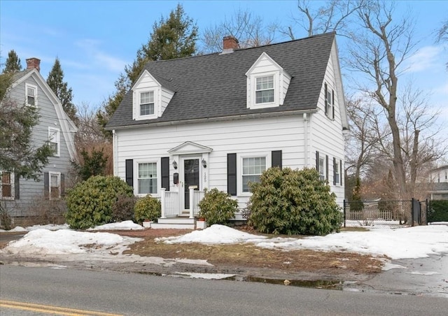 cape cod-style house featuring fence, a chimney, and a shingled roof