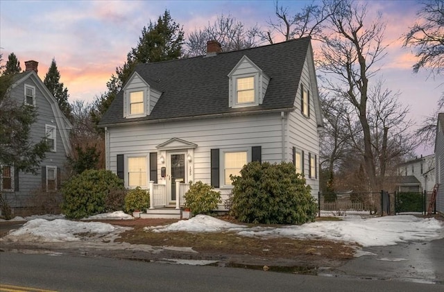 cape cod-style house with fence, roof with shingles, and a chimney