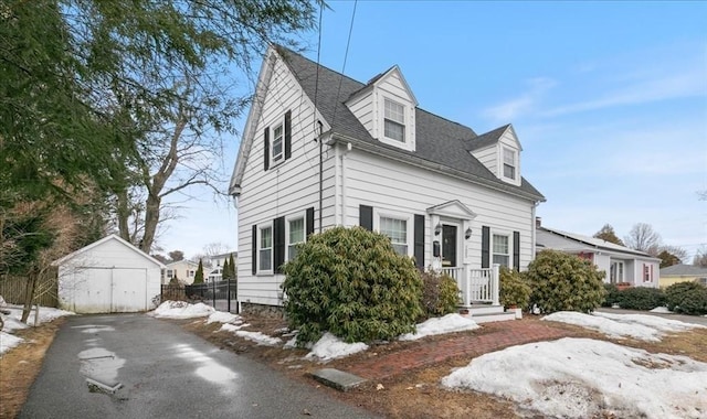 new england style home featuring an outdoor structure, a garage, a shed, and a shingled roof