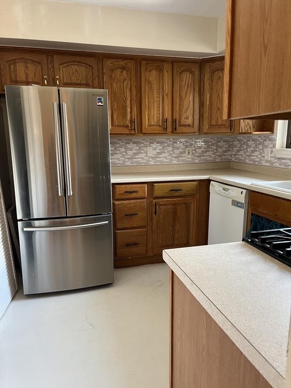 kitchen featuring brown cabinetry, freestanding refrigerator, light countertops, and white dishwasher