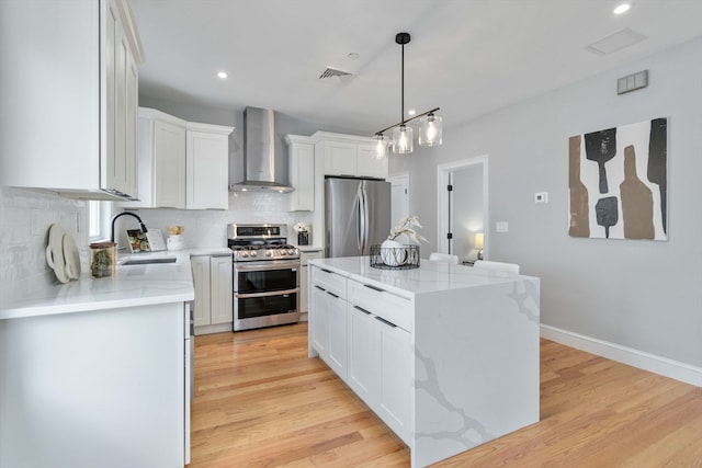 kitchen with wall chimney exhaust hood, light hardwood / wood-style flooring, stainless steel appliances, a center island, and white cabinetry