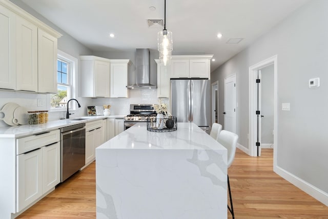 kitchen featuring sink, a kitchen island, wall chimney exhaust hood, stainless steel appliances, and light wood-type flooring