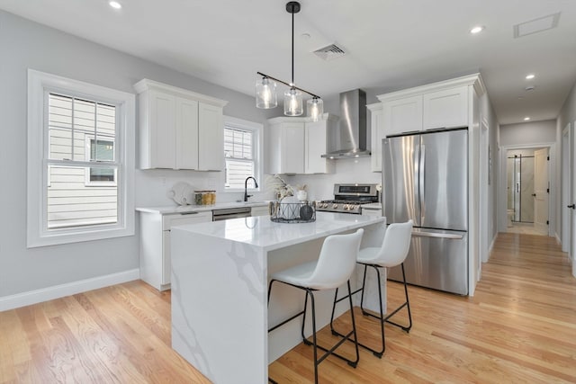 kitchen featuring stainless steel appliances, wall chimney exhaust hood, white cabinetry, and a kitchen island