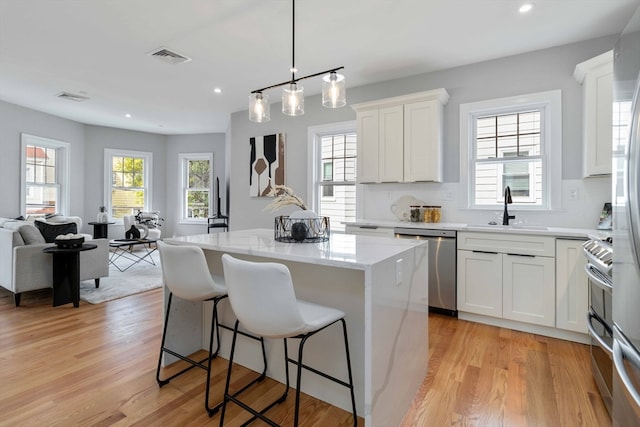 kitchen featuring white cabinets, stainless steel appliances, light hardwood / wood-style floors, and a kitchen island