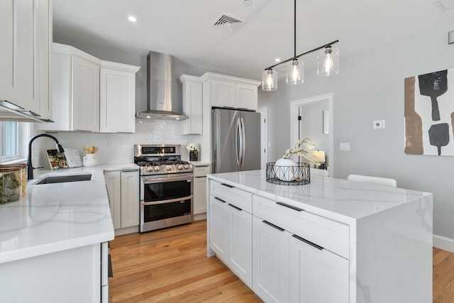 kitchen featuring a center island, light hardwood / wood-style floors, wall chimney range hood, white cabinetry, and appliances with stainless steel finishes