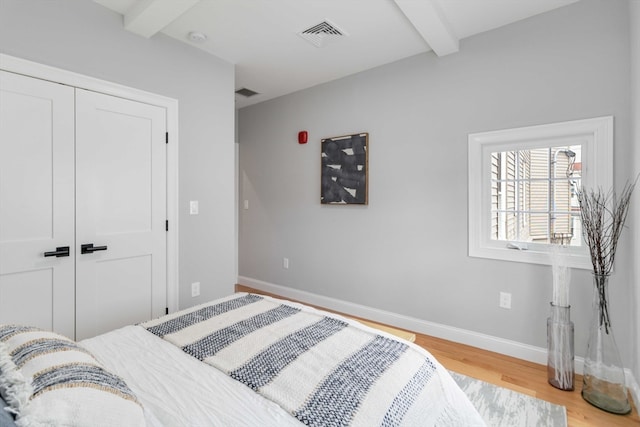 bedroom with a closet, beamed ceiling, and light hardwood / wood-style floors