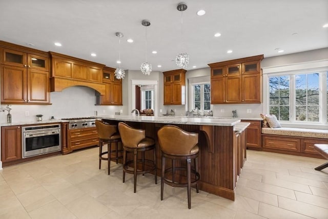 kitchen with appliances with stainless steel finishes, light stone counters, a healthy amount of sunlight, decorative light fixtures, and a kitchen island