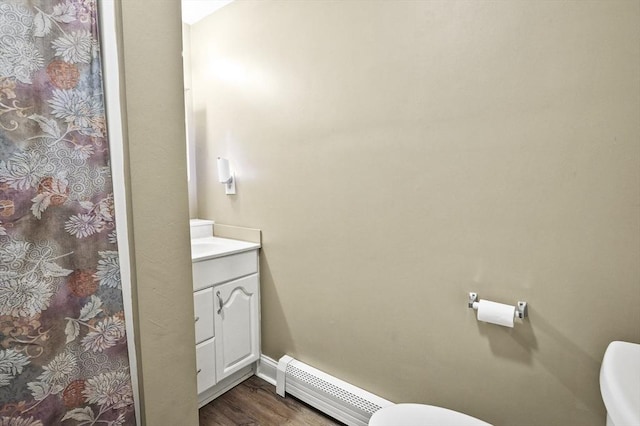 full bath featuring toilet, wood finished floors, a baseboard heating unit, vanity, and curtained shower