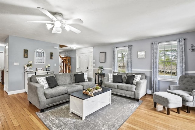 living area featuring light wood-type flooring, stairway, baseboards, and a ceiling fan