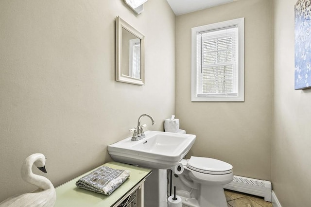 bathroom featuring baseboard heating, toilet, baseboards, a sink, and tile patterned flooring