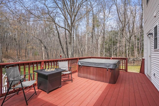 wooden terrace featuring a hot tub, an outdoor fire pit, and a view of trees