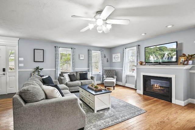 living room featuring a ceiling fan, recessed lighting, baseboards, light wood finished floors, and a glass covered fireplace