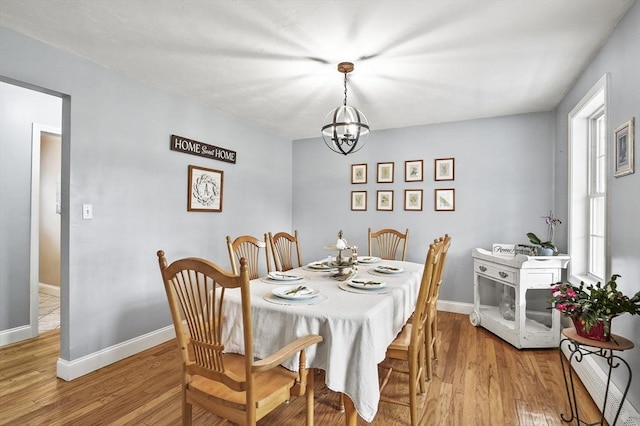 dining room with light wood-style flooring, a notable chandelier, and baseboards