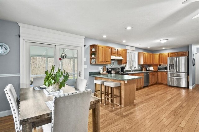 kitchen featuring under cabinet range hood, brown cabinetry, a sink, a peninsula, and stainless steel appliances