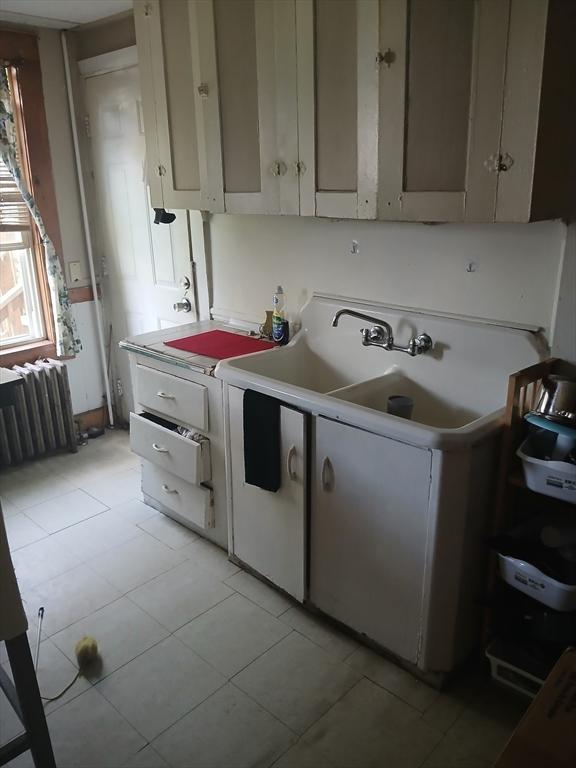 kitchen with light tile patterned floors, radiator, light countertops, and white cabinets