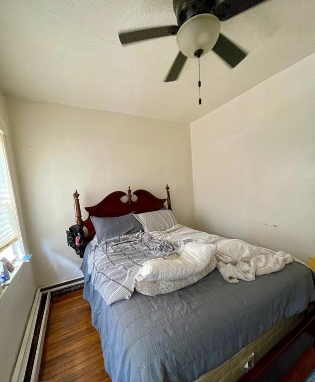 bedroom with wood finished floors, baseboard heating, and ceiling fan