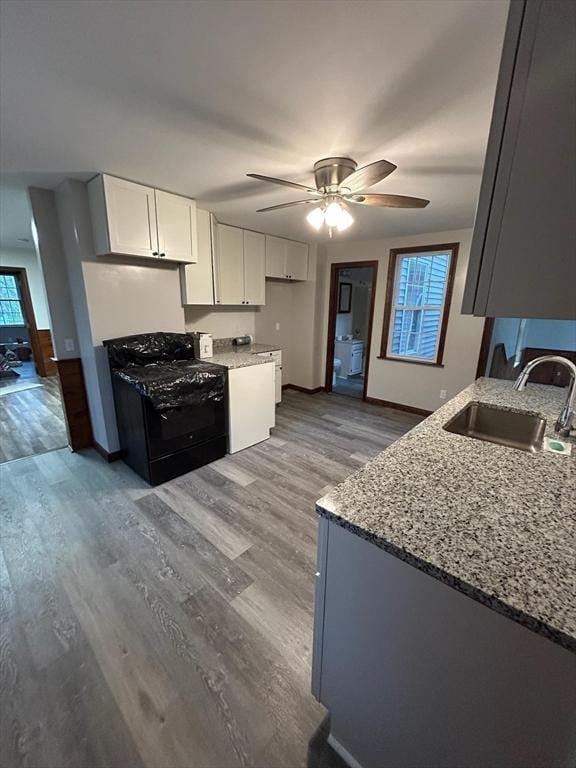 kitchen featuring white cabinetry, hardwood / wood-style floors, black range oven, light stone countertops, and sink