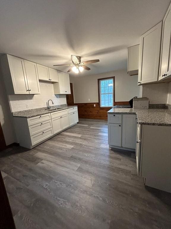 kitchen with white cabinetry, wooden walls, ceiling fan, sink, and hardwood / wood-style flooring