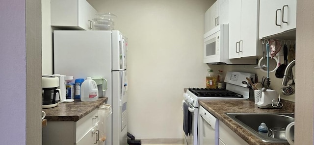 kitchen featuring white appliances, dark countertops, white cabinets, and a sink