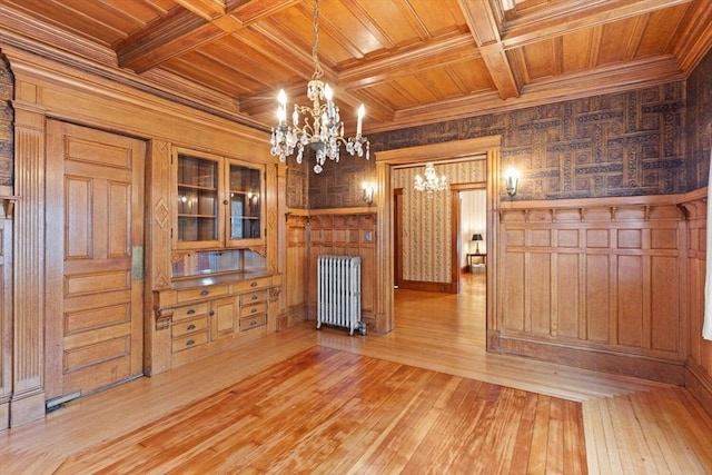 unfurnished dining area featuring wooden walls, a chandelier, radiator heating unit, wooden ceiling, and light wood-type flooring