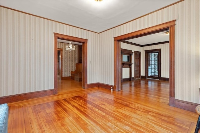 empty room with baseboards, an inviting chandelier, ornamental molding, and light wood-type flooring