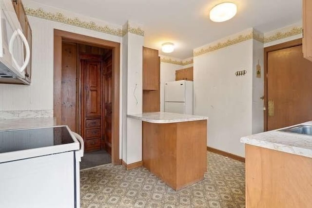 kitchen featuring white appliances, a peninsula, baseboards, and light countertops