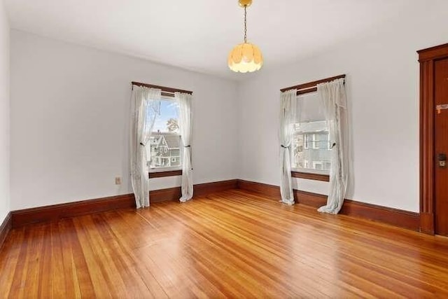 spare room with baseboards, light wood-style flooring, and a healthy amount of sunlight
